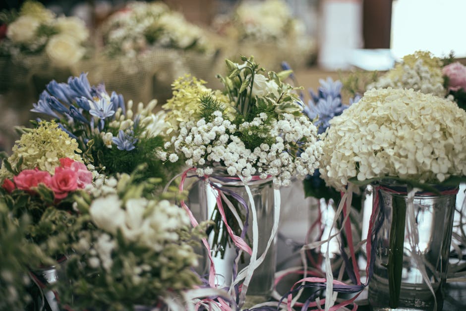A collection of floral arrangements in clear glass vases, featuring a variety of fresh flowers such as white hydrangeas, pink roses, bluebell-like flowers, and white baby's breath, all arranged in a l