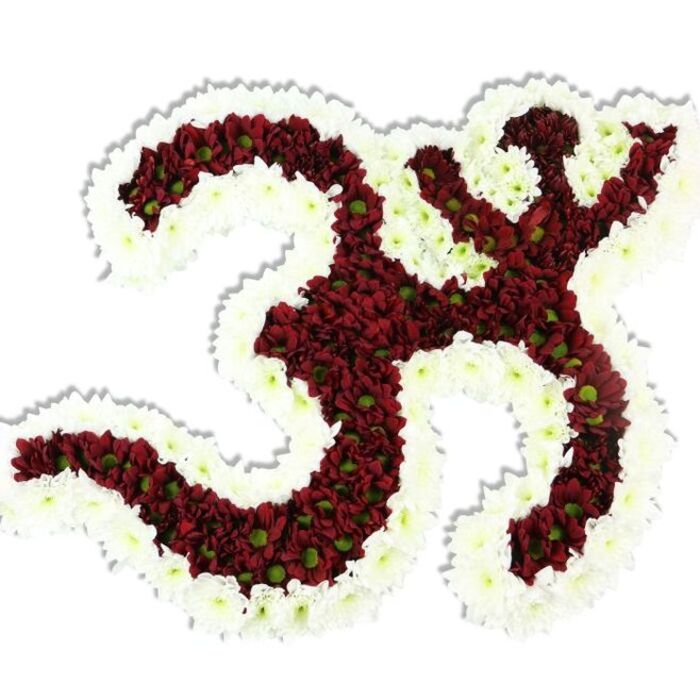 Against a clean white background, a finely modelled Om (Aum) symbol is articulated entirely from tightly clustered, small-headed chrysanthemums, the central planes filled with deep maroon or burgundy pompon flowers. The arrangement traces every stroke-the threefold curve, the sweeping downward arm and the small crescent and dot above-with a dense layering of blooms so compact they form a soft, velvety relief. Many of the dark red blooms reveal a contrasting lime-green eye at their centres, which breaks up the maroon field with delicate flecks of freshness and natural texture. A voluptuous outline of pristine white spray chrysanthemums frames the symbol, sculpting its negative spaces and giving the motif a luminous edge that reads like a carved silhouette on a gallery wall. The composition is built to be seen closely yet respected from afar: petals overlap with deliberate regularity, stems are secured beneath to hold the sculptural curve, and a faint drop shadow beneath the piece confirms its dimensional weight beneath studio lighting. Imagine the faint, grounding scent of chrysanthemums and a cool, silky touch across the surface-the sensory cues an experienced florist leans on when composing for sacred occasions. This floral Om is intended for spiritual observances, remembrance services, or cultural celebrations around Fortis Green, Muswell Hill and nearby Highgate, where its measured beauty and dignified presence will both comfort and centre attendees in moments of reflection.