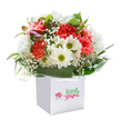 Overflowing with joy and sincerity, this floral arrangement captures the essence of a Fortis Green celebration, artfully presented in a spotless white square gift bag. The bouquet is an uplifting display of coral and blush carnations, their softly ruffled petals sensuous to the touch and reminiscent of late-spring blossoms peeking through the gardens near Fortis Green's leafy lanes. Mixed with these are cheerful white daisies, their sunny greenish-yellow centers shining bright, accompanied by sprigs of delicate baby's breath that twinkle like tiny stars amidst the blooms. Subtle hints of unopened buds add intrigue, with purple and pink at their tips promising future beauty. Framing the bouquet are generous sprays of glossy, deep green leaves, creating a lush and cradling effect around the flowers, as if protecting a precious secret. The sturdy gift bag, with its sleek handles, enhances ease of gifting-a nod to the convenience cherished by locals. Each element is expertly positioned, resulting in a harmonious mix that feels both spontaneous and thoughtfully planned. This bouquet embodies new beginnings, heartfelt congratulations, or simply a wish to bring a little sunlight into someone's day in Fortis Green, all with the expert touch and local love that defines this unique neighbourhood.